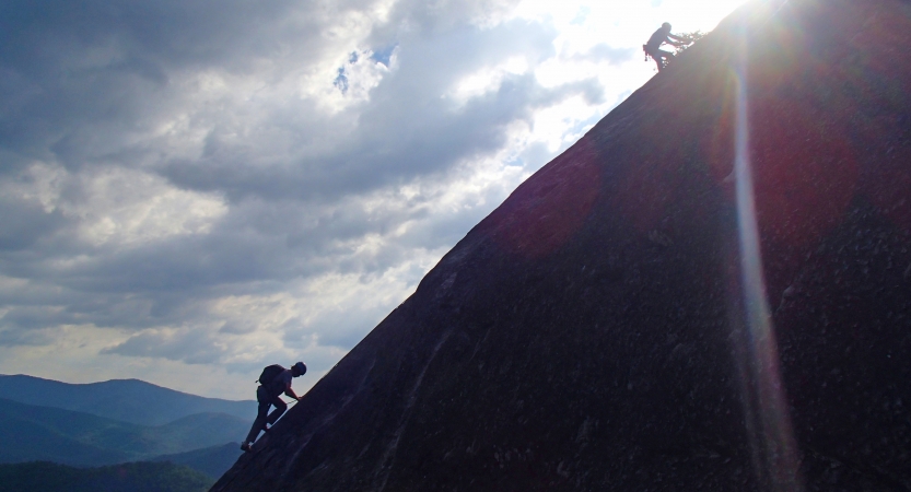 two people ascend up a sloped rock